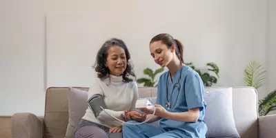 Eine Pflegehilfskraft erledigt das Blutdruckmessen